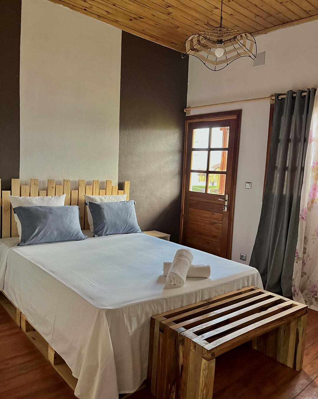 Chambre avec lit double, plafond en bois et porte vitrée donnant sur le jardin